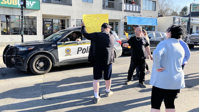 Des manifestants, dans une rue, près d'un véhicule de police.