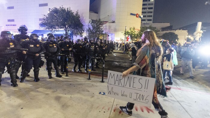 Un manifestant fait face à des dizaines de policiers en tenue antiémeute dans la rue et tient une pancarte où l'on peut lire «Marines!! Où étiez-vous le 6 janvier».