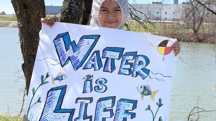 Une jeune fille tient une pancarte sur laquelle est écrit que l'eau est la vie.