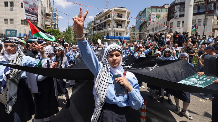 Un groupe de manifestants défile dans une rue, certains agitant des drapeaux palestiniens.