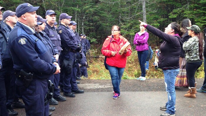 Une femme, debout devant des policiers, pointe au loin.