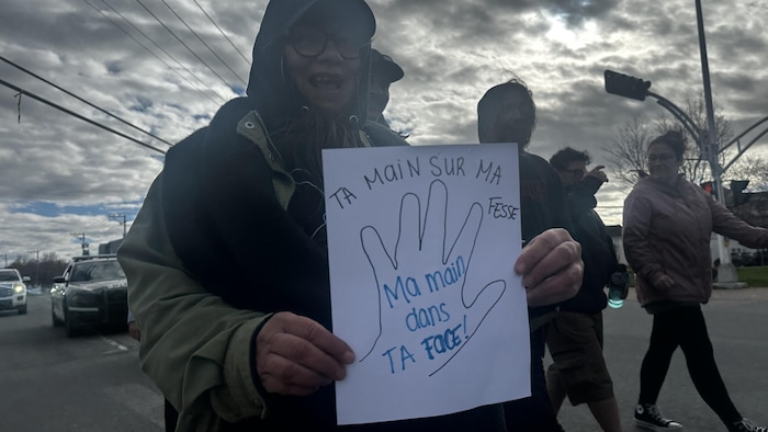 Une femme tient une affiche avec inscrit « ta main sur ma fesse, ma main dans ta face! ».