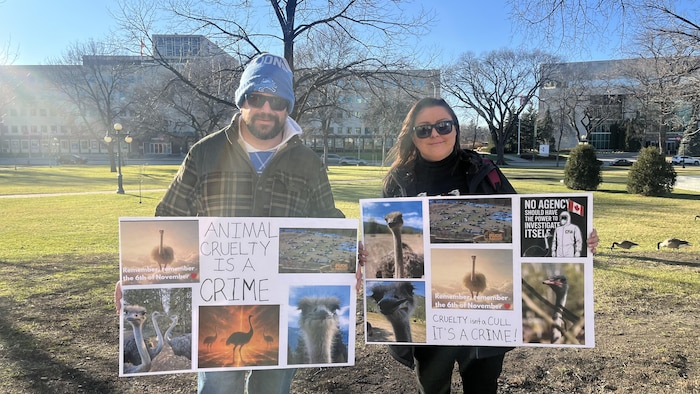 Deux personnes tiennent, l'une à côté de l'autre, des pancartes dénonciatrices sur lesquelles on voit en gros caractères le mot « crime », le 22 novembre 2025 à Winnipeg. 