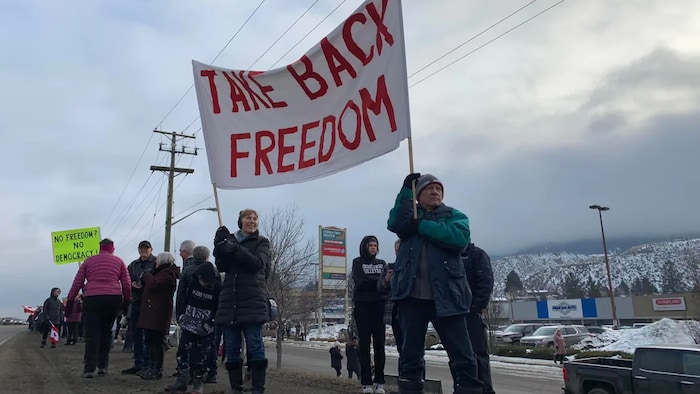 Anti-vaccine-mandate protesters in Kamloops, B.C., hold up a sign supporting the cross-country rally against a federal vaccine mandate for truckers crossing the U.S.-Canada Border. 