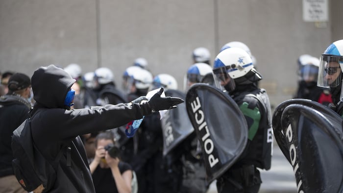 Des policiers munis de casques et de boucliers devant des manifestants.