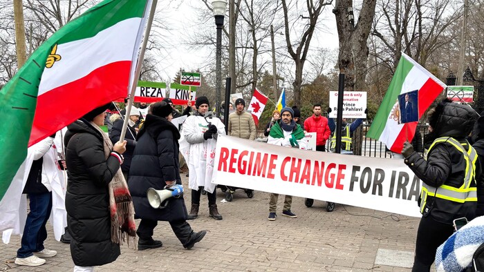 Des manifestants arrêtés sur un trottoir, avec une longue bannière horizontale où est écrit «Regime Change for Iran», des drapeaux iraniens, et des messages appuyant Reza Pahlavi.