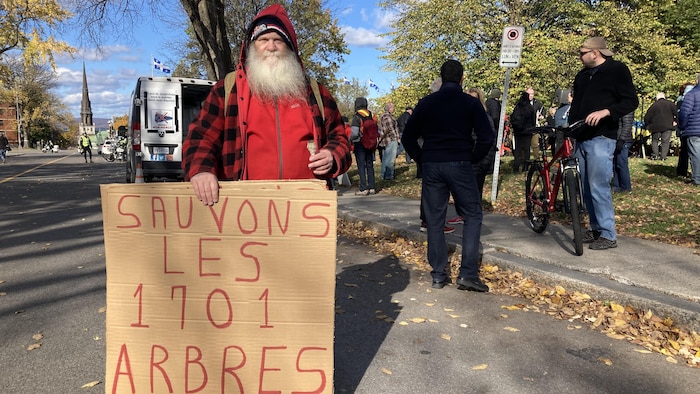 Un citoyen avec une longue barbe présente sa pancarte avec la phrase «Sauvons les 1701 arbres» lors d'une manifestation.