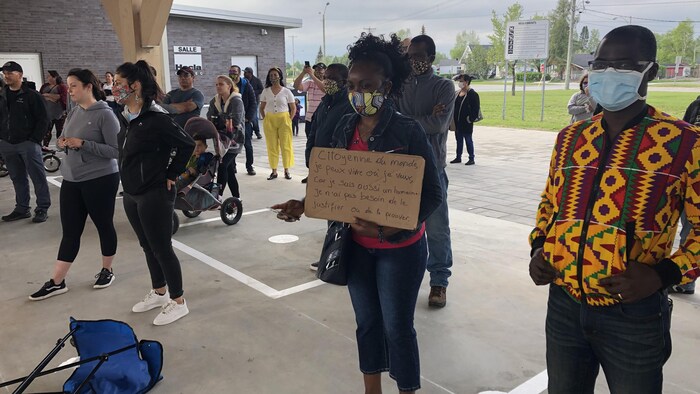 Des citoyens sont réunis pacifiquement, dont une femme tenant une affiche où il est écrit : citoyenne du monde.
