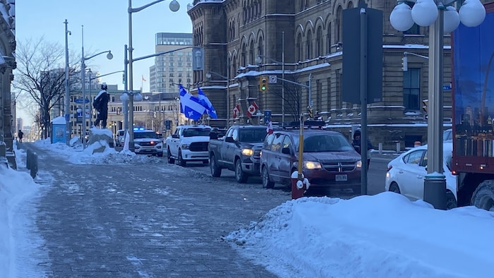 Des camions stationnés dans une rue, dont l'un porte un drapeau du Québec.