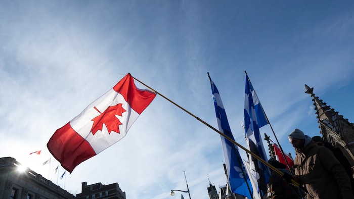 Des drapeaux du Canada et du Québec tenus par des manifestants.