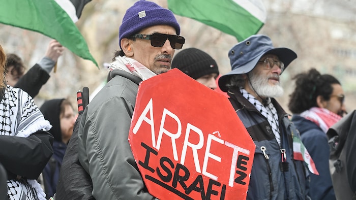 Un manifestant tient une pancarte en forme de panneau d'arrêt qui porte la mention « Arrêtez Israël ».