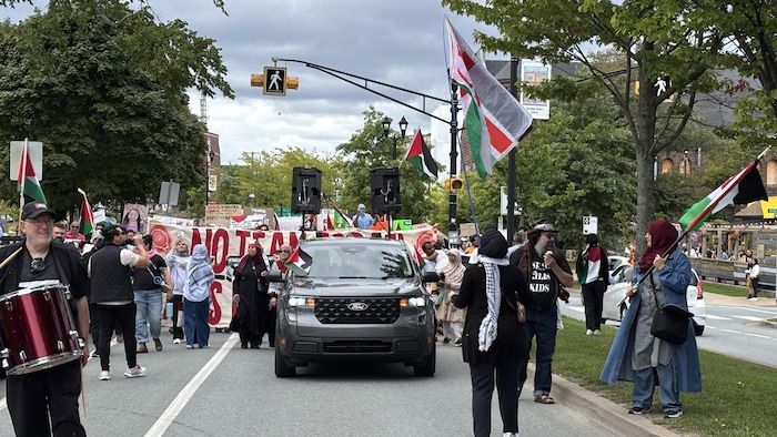 Des gens défilent dans la rue derrière une bannière où connected  a peint en rouge la operation   «No Team Israel Tennis Players successful  Halifax». Plusieurs ont des drapeaux de la Palestine.