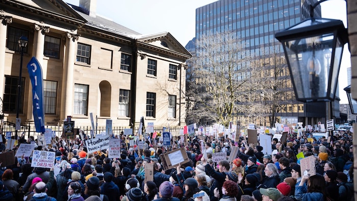 Une foule de plusieurs centaines de personnes, agitant des affiches, obstrue complètement une rue devant Province House.