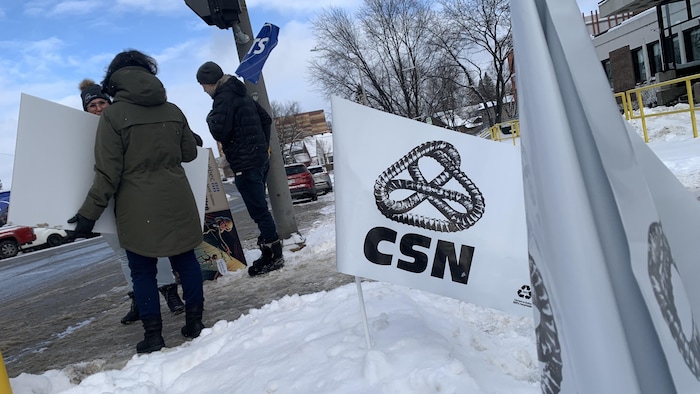 Plusieurs personnes tiennent des banderoles et des drapeaux en main manifestent dehors en hiver. 