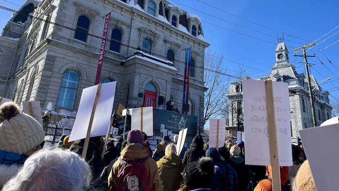 Des gens avec des pancartes regardent en direction du Musée des beaux-arts de Sherbrooke.