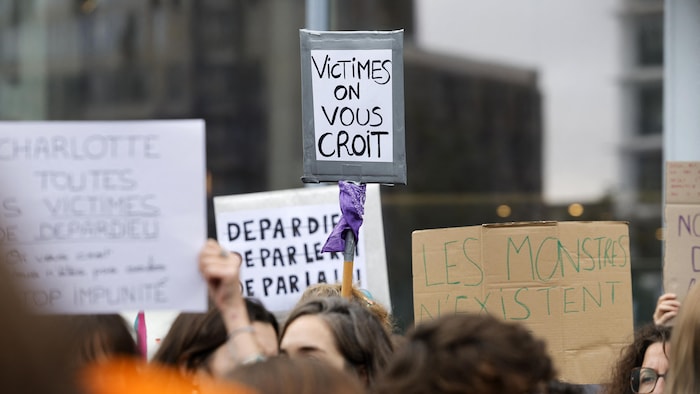 Un manifestant tient une pancarte sur laquelle on peut lire «Victimes, on vous croit».