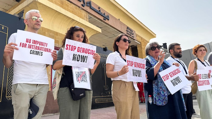 Des députés italiens et européens brandissent des pancartes lors d'une manifestation devant le côté égyptien du poste-frontière de Rafah, appelant à « mettre fin au génocide » dans la bande de Gaza, le 18 mai 2025.
