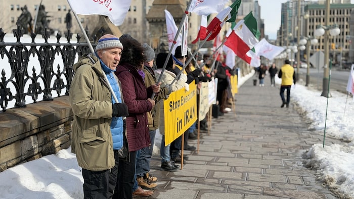 Des personnes sont alignées avec des drapeaux et des pancartes sur lesquelles on peut lire, notamment, « Arrêtez les exécutions en Iran » en anglais.