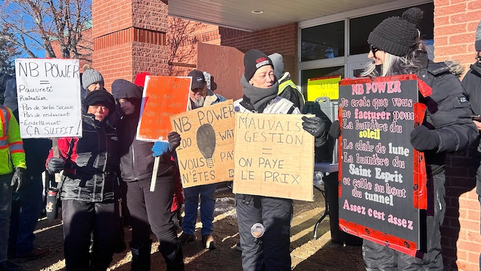 Chaudement habillés pour l'hiver, des manifestants devant un édifice présentent les pancartes qu'ils ont préparées.