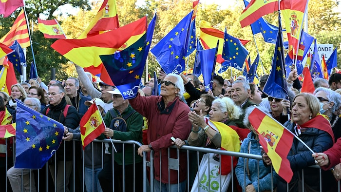 Pessoas manifestando-se carregando bandeiras espanholas atrás de uma barricada.