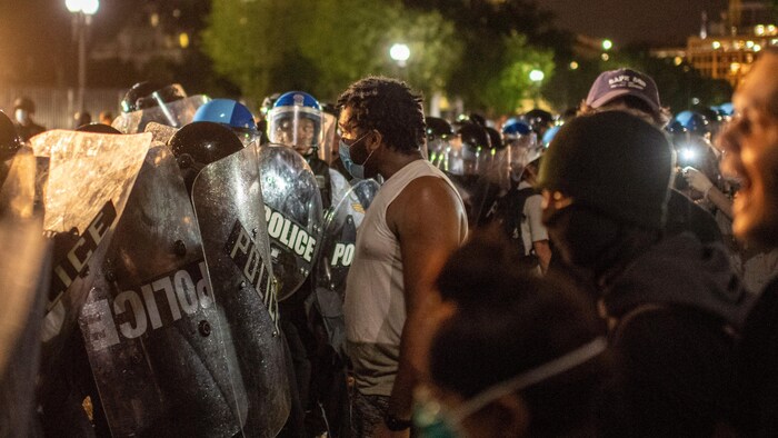Un homme noir fait face à une lignée de policiers anti-émeutes.