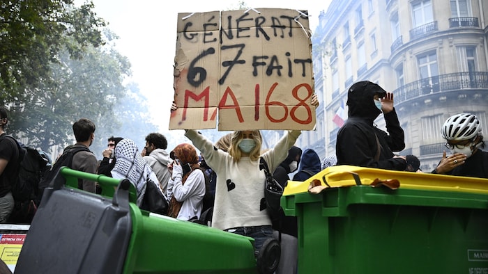 Une femme blonde manifeste dans les rues de Paris en tenant une pancarte où on peut lire « Génération 6 7 fait Mai 68 »