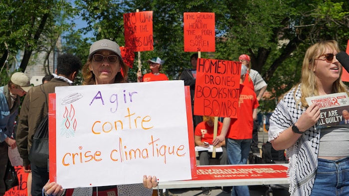 Une personne brandit une pancarte sur laquelle on peut lire « Agir contre la crise climatique ».