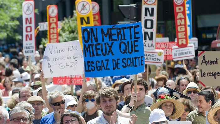 Une foule manifeste dans la rue avec des pancartes écrites à la main dénonçant l'exploitation des gaz de schiste.