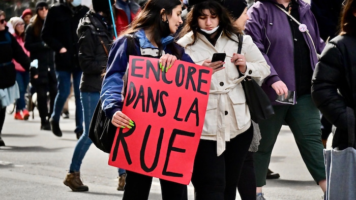 Une jeune femme tient une pancarte sur laquelle on peut lire : « Encore dans la rue ».