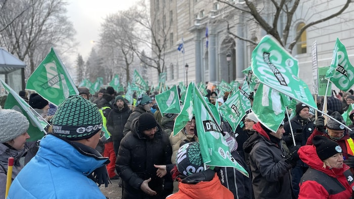 Une foule de manifestants brandissant des drapeaux aux couleur du Front commun intersyndical en hiver devant l'Assemblée nationale.