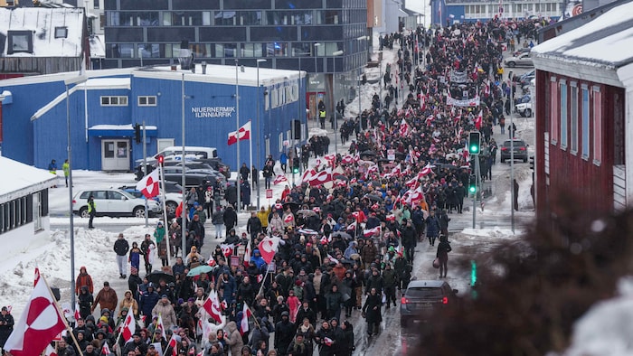 Une foule de personnes marche dans une rue, certaines agitent un drapeau du Groenland.