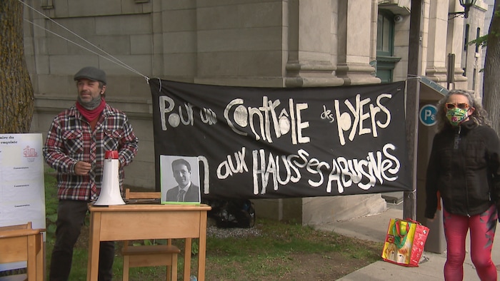 Deux manifestants se tiennent de part et d'autre d'une banderole sur laquelle il est écrit : «Pour un contrôle des loyers. Non aux hausses abusives.»