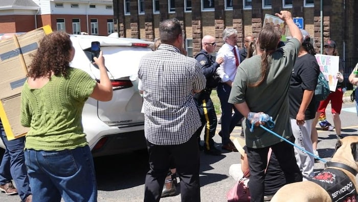 Tim Houston escorté par la police devant des manifestants hostiles.