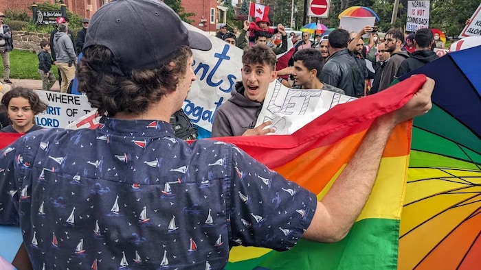 Des manifestants, dont un tient un drapeau multicolore, s'invectivent.
