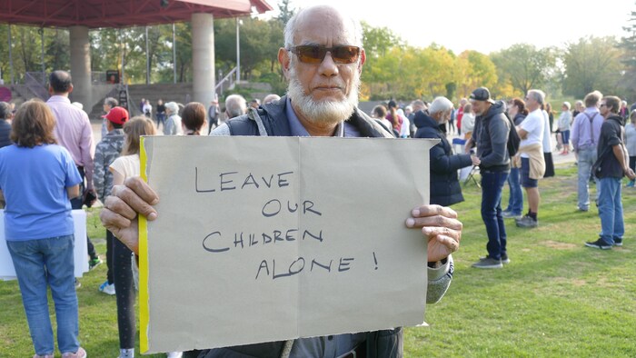 Un homme qui tient une pancarte sur laquelle on peut lire « Laissez nos enfants tranquilles ».