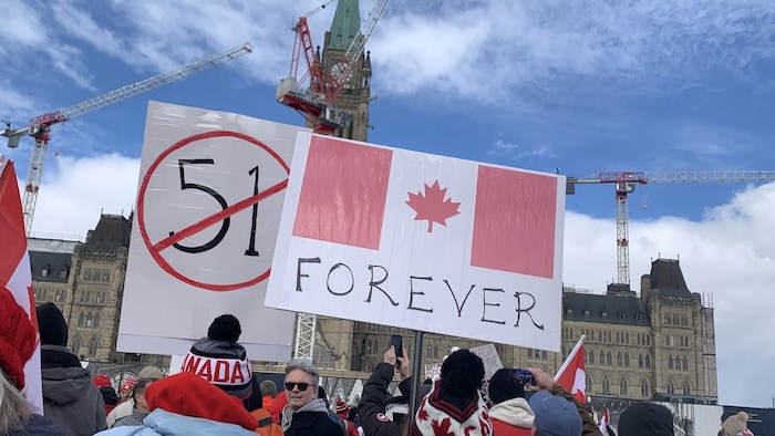 Des gens tiennent des pancartes lors d'une manifestation devant le parlement à Ottawa en plein hiver.