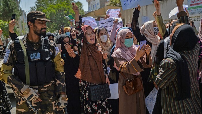 Des femmes manifestent tout près d'un combattant taliban.