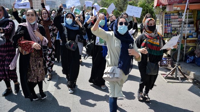 Des femmes marchent dans une rue. Plusieurs brandissent un poing en l'air. Leur visage n'est pas voilé, mais beaucoup d'entre elles portent un masque. 