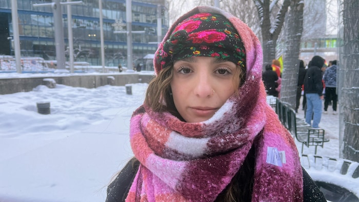 Une jeune femme portant un piercing au nez, la tête enveloppée d'un foulard noir à fleurs roses et une épaisse écharpe en laine aux dégradés de rose et de violet.