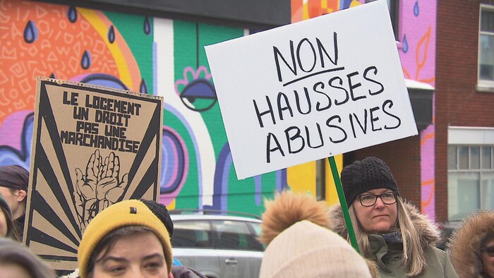 Des gens qui tiennent des pancartes devant une murale de Trois-Rivières.
