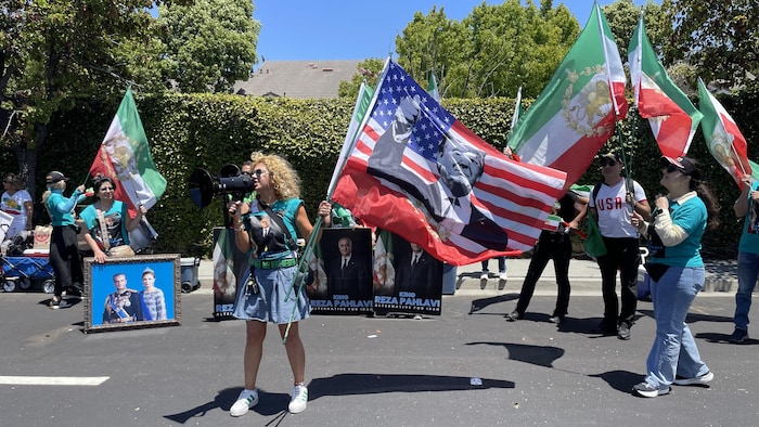 Une femme brandissant le drapeau des États-Unis sur lequel figure le portrait du président Trump appelle à la reprise de la guerre contre l'Iran avant le match de l'équipe iranienne de soccer à Los Angeles.
