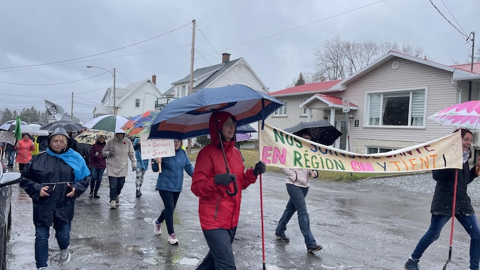 Des citoyens tiennent des pancartes et des banderoles et marchent dans les rues de Témiscouata-sur-le-Lac.