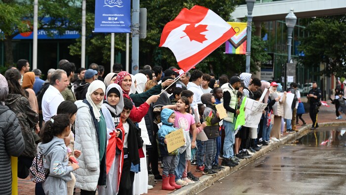 Une foule de manifestants, dont une personne qui tient un drapeau du Canada.