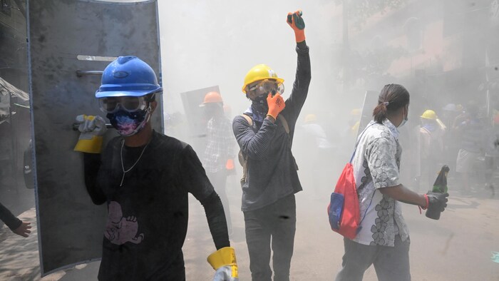 Gros plan sur trois manifestants qui se couvrent le visage en raison des gaz lacrymogènes. 