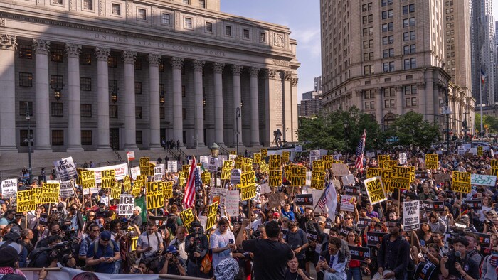 Devant un palais de justice, une foule de manifestants, dont plusieurs tiennent des pancartes disant « ICE à l'extérieur de NY » et « Arrêtez les expulions maintenant! ». 