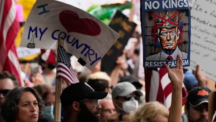 Une foule compacte de manifestants tenant des drapeaux des États-Unis et des affiches, l'une avec le message en anglais « J'aime mon pays », l'autre « Pas de rois, résistez au fascisme » avec une illustration de Donald Trump portant une couronne, laquelle est marquée d'une croix rouge.