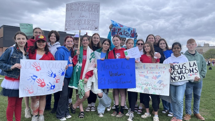 Des élèves avec des pancartes lors d'une manifestation pour une nouvelle école secondaire francophone à Cornwall le 23 mai 2025.