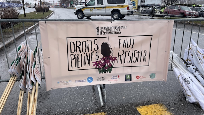 Une pancarte de la Journée internationale des travailleuses et des travailleurs posée sur une barrière anti-émeute, devant l'hôtel Universel.