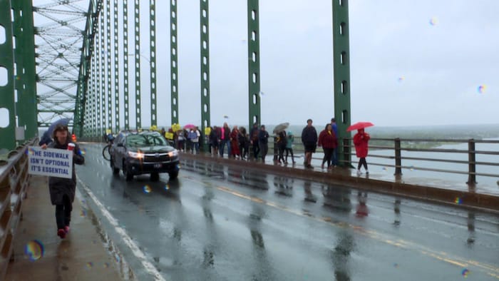 Des gens marchent sur les trottoirs de chaque côté du pont en brandissant des pancartes.
