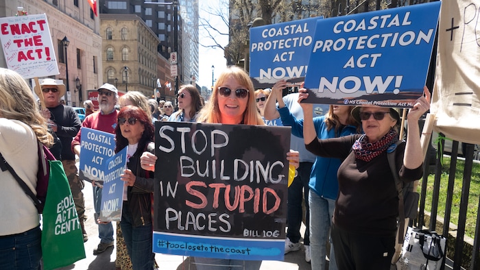 Une manifestante tient une pancarte sur laquelle est écrit « arrêtez de construire dans des endroits stupides ». 